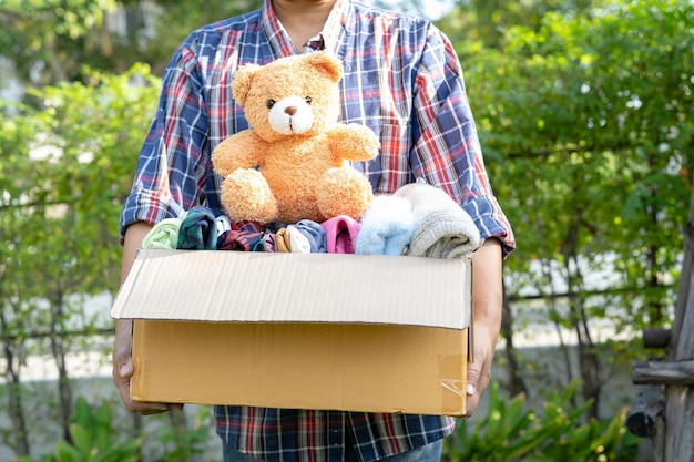 Holding clothing donation box with used clothes and doll at home to support help for poor people in the world