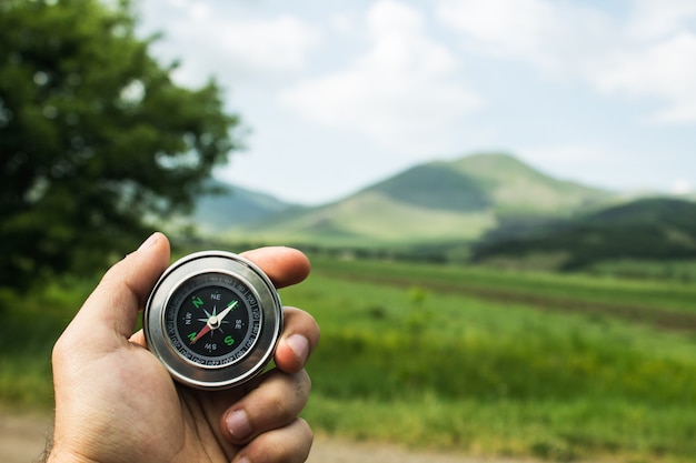 Holding a compass against the background of a green field during the day