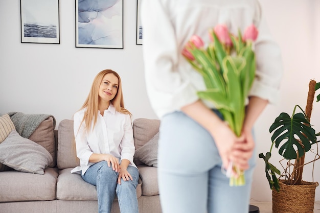 Holding flowers Young mother with her daughter is at home at daytime