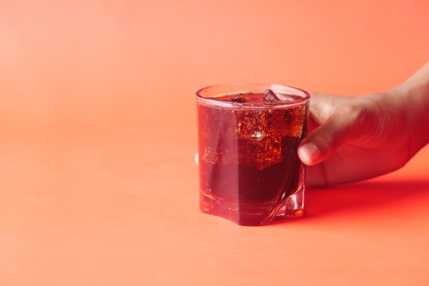 Holding a glass of soft drink on red background