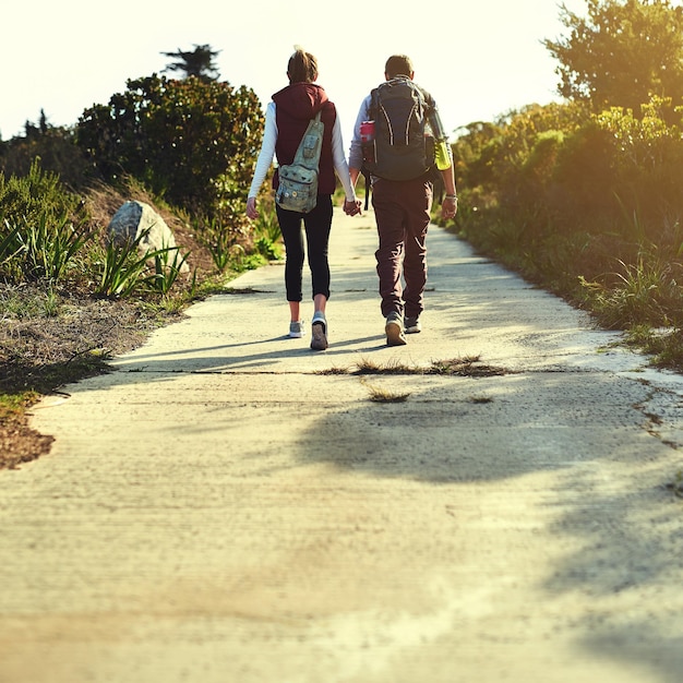 Photo holding hands back or couple hiking for travel outdoor adventure or journey in forest nature or woods love wellness or people on path walking together for holiday or trekking to explore in park