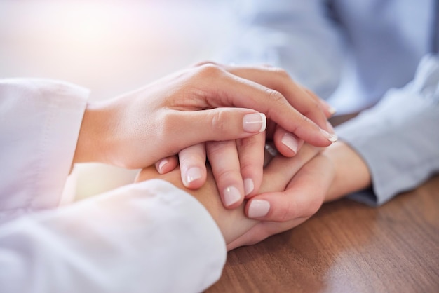 Holding hands doctor and patient at desk for comfort talking and communication for bad news mental health or support Therapist woman cancer and together for empathy care or wellness in hospital