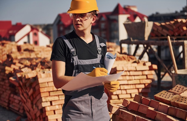 Holding plan in hands Construction worker in uniform and safety equipment have job on building