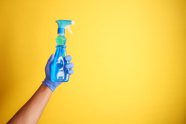 Holding a plastic cleaning bottle against yellow background