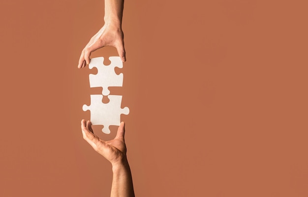 Holding puzzle Business solutions success and strategy concept Two hands trying to connect couple puzzle piece on gray background Teamwork concept Closeup hand of connecting jigsaw puzzle