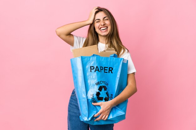 Holding a recycling bag full of paper to recycle over isolated pink laughing