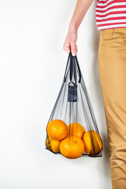 Holding a reusable string bag full of oranges.