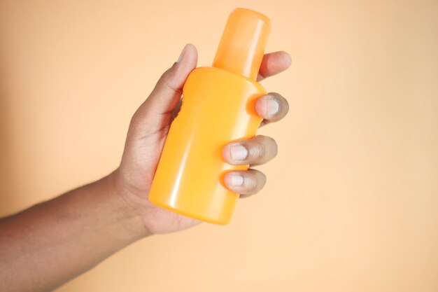 holding a sunscreen cream against orange background