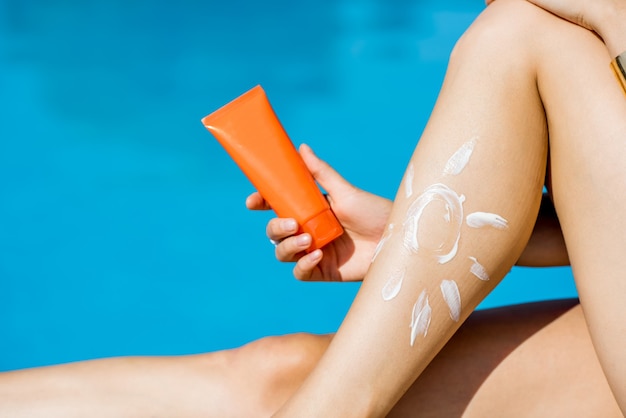 Photo holding sunscreen lotion tube near the legs on the blue water background. sunscreen solar cream uv protection concept