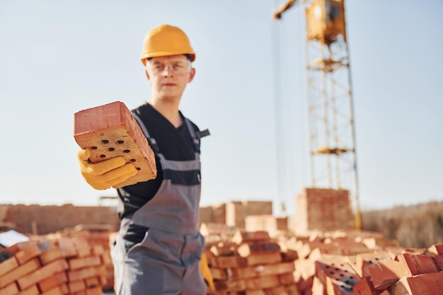 Holds brick in hand Construction worker in uniform and safety equipment have job on building