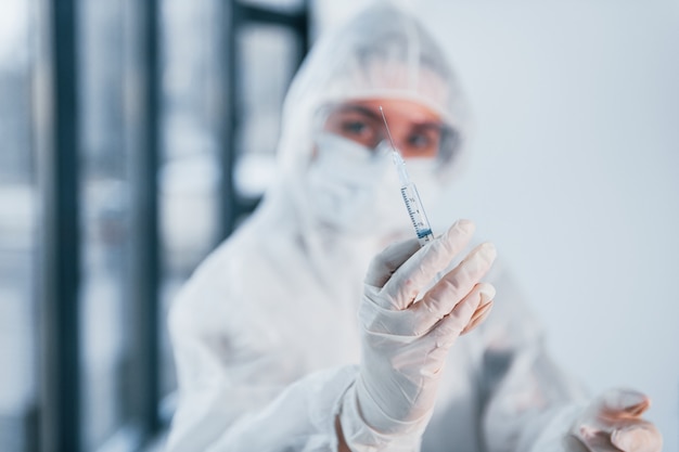 Holds syringe. Portrait of female doctor scientist in lab coat, defensive eyewear and mask