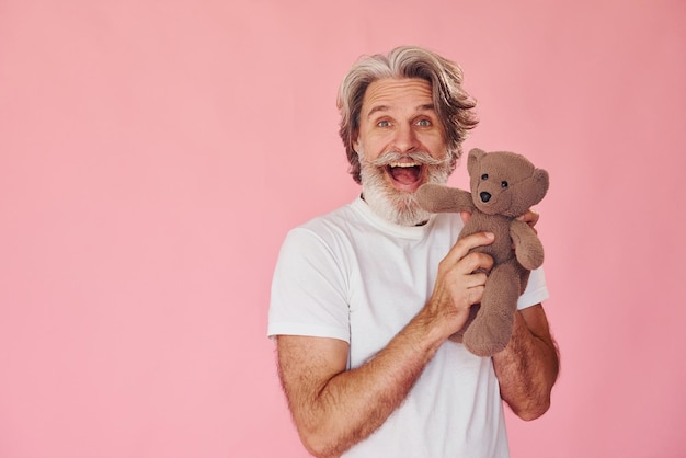 Holds teddy bear Stylish modern senior man with gray hair and beard is indoors