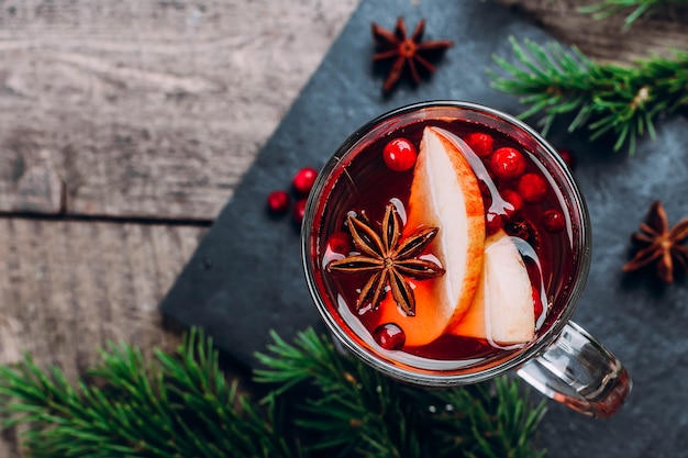 Holiday Hot Drink. Mulled Wine In Glass with Spices And Apple on Wooden Table