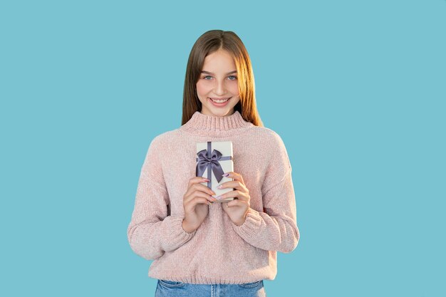 Photo holiday present festive gift special occasion greeting portrait of happy satisfied teen girl holding wrapped box with ribbon bow smiling looking at camera isolated on blue empty space background