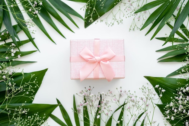 Holiday present Floral composition Pink gift box with ribbon bow in green leaf frame isolated on white Natural arrangement Festive background