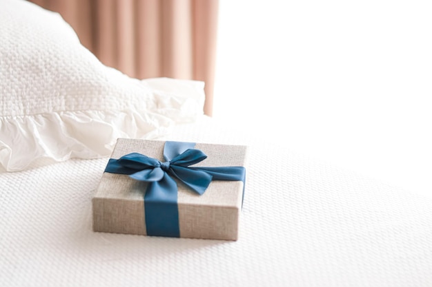 Holiday present and luxury online shopping delivery wrapped linen gift box with blue ribbon on bed in bedroom chic countryside style