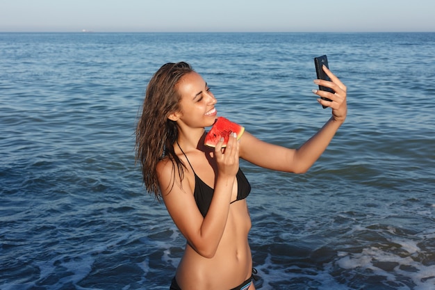 Holiday, resort, tourism concept - Summer vacation - young girl eating fresh watermelon on sandy beach. young beautiful woman eats watermelon on the beach at hot summer day.