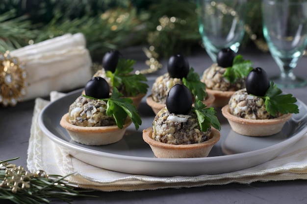 Holiday snack in tartlets with mushrooms egg and black olives on a gray background