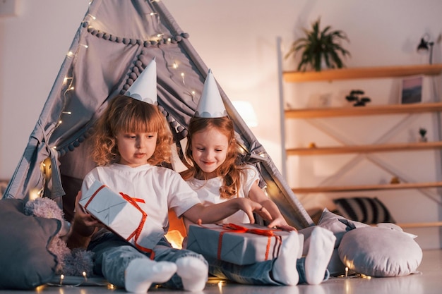 Photo holiday surprise with gift boxes two little girls is in the tent in domestic room together