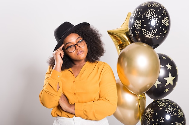 Holidays, birthday party and fun concept - Portrait of smiling young African-American young woman looking stylish on white background holding balloons.