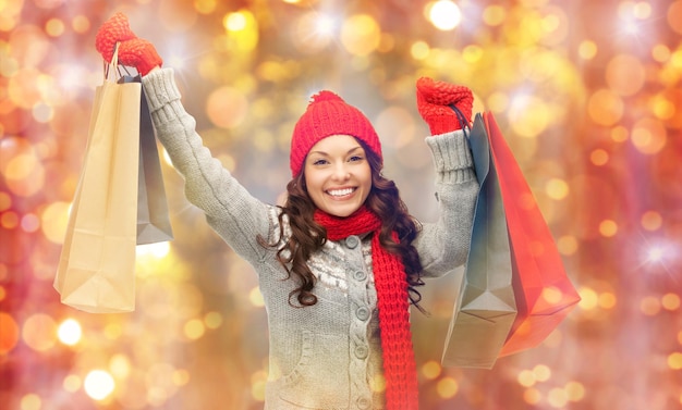 holidays, christmas, sale and people concept - happy smiling young asian woman in winter clothes with shopping bags over lights background