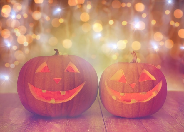 holidays, halloween and decoration concept - close up of carved pumpkins with smiley faces on table over lights