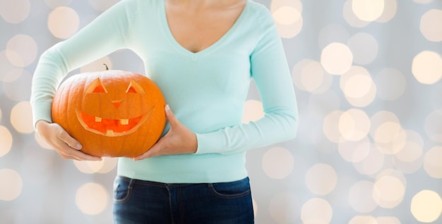 holidays, halloween, decoration and people concept - close up of woman with carved pumpkin