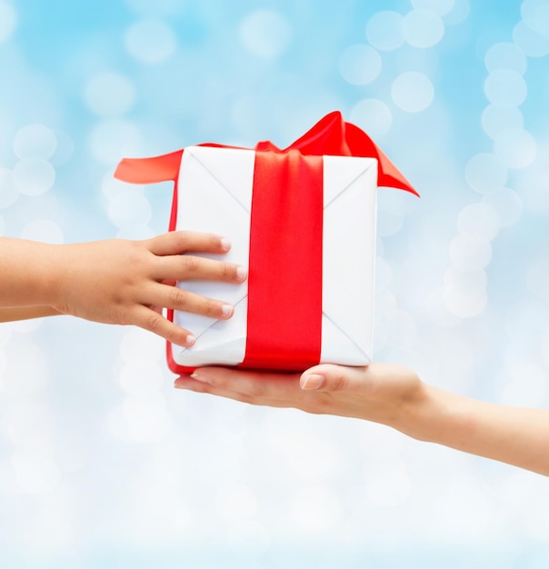 holidays, present, christmas, childhood and happiness concept - close up of child and mother hands with gift box over blue lights background