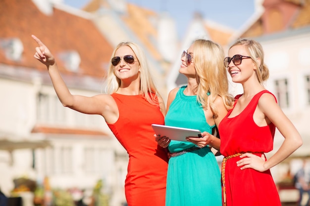 holidays and tourism concept - beautiful blonde girls toursits looking into tablet pc in the city