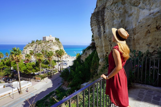 Holidays in Tropea Back view of beautiful fashion girl enjoying view of the Monastery of Santa Maria dell'Isola of Tropea Summer vacation in Italy