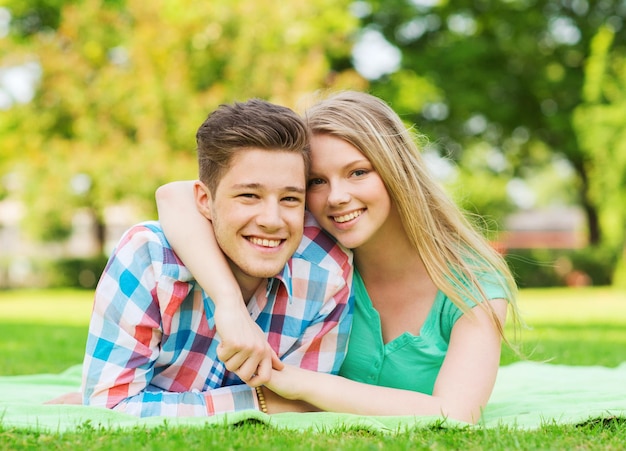 holidays, vacation, love and friendship concept - smiling couple lying on blanket in park