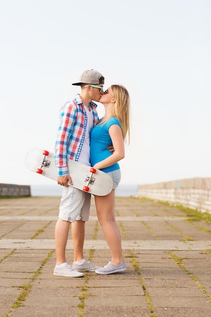 Photo holidays, vacation, love and friendship concept - smiling couple with skateboard kissing outdoors