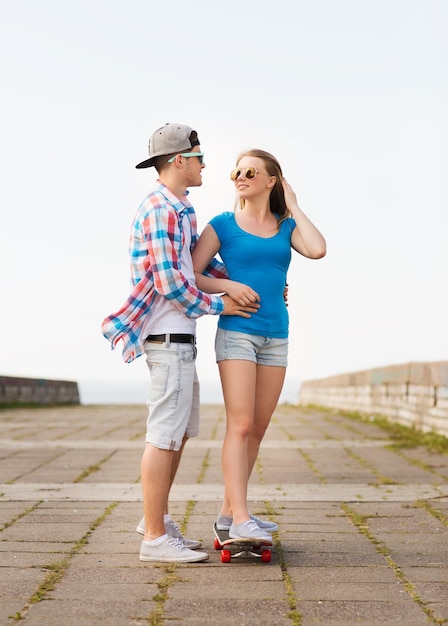 holidays, vacation, love and friendship concept - smiling couple with skateboard outdoors