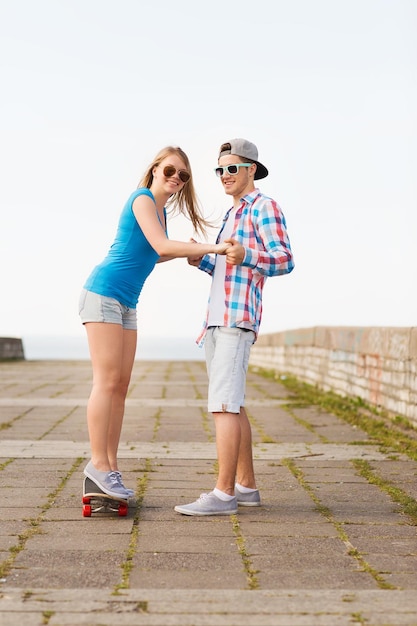 holidays, vacation, love and friendship concept - smiling couple with skateboard riding outdoors