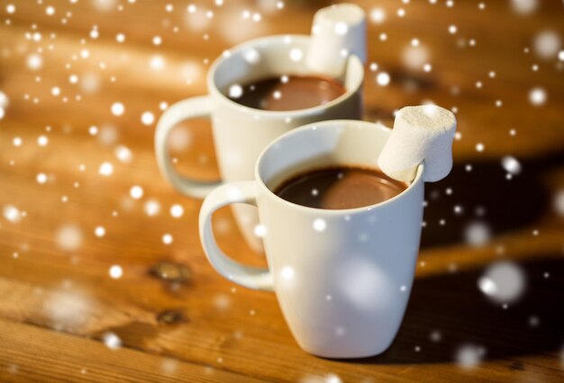 holidays, winter, food and drinks concept - close up of cups with hot chocolate or cocoa drinks and marshmallow on wooden table