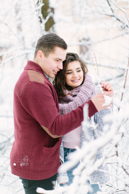 Holidays, winter, , hot drinks and people  - happy couple in warm clothes hugging near the tree branches with snow