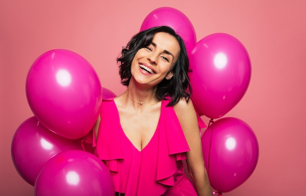 Hollywood smile. Close-up photo of a young charming lady in a pink dress, who is laughing out of joy, surrounded by pink balloons.