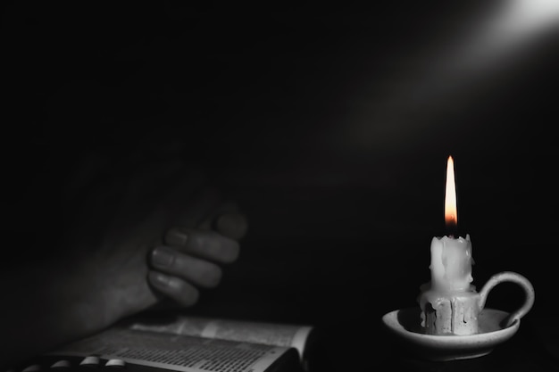 Holy bible and praying man's hands and burning candle background with bright rays of light