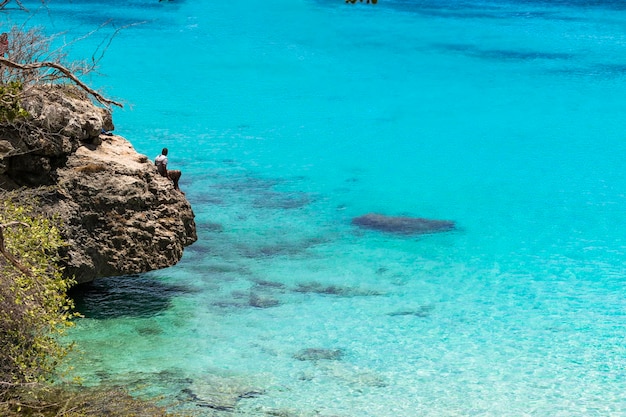 Hombre sentado a la orilla del mar caribe sobre una enorme roca divizando el paisaje