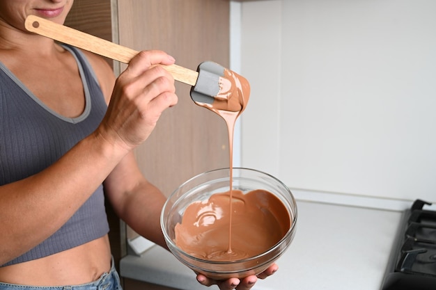 Home confectioner cooking dessert Woman tempering chocolate Closeup stirring milk melted chocolate in glass bowl