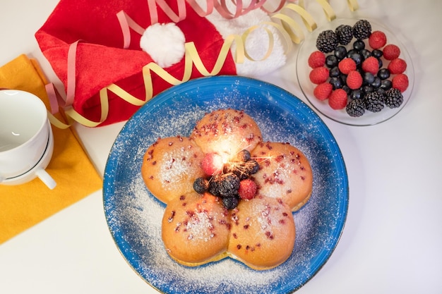 Home cooking concept Fresh organic homemade sweet soft milk bread filled with cream and decorated with berries on blue dish Christmas holiday with sparkling light and Santa Claus hat