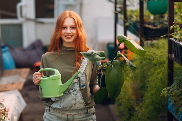 Home gardening concept young woman with green watering can planting plants floral in greenhouse garden at home