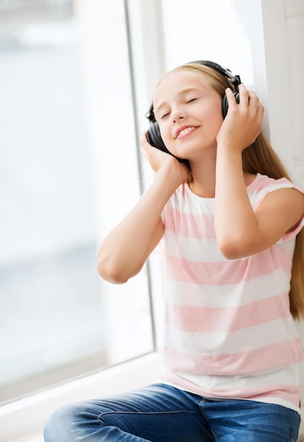 home, leisure, new technology and music concept - little girl with headphones at home