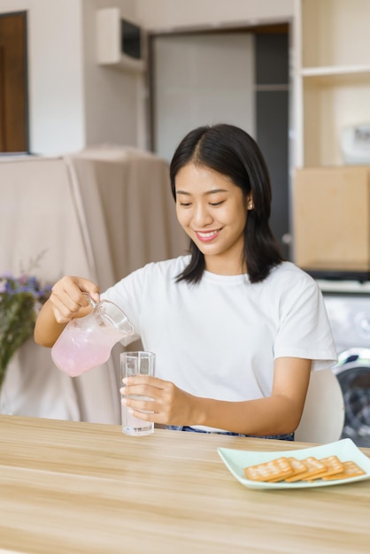 Home lifestyle concept Young woman pour water from jug into glass while having snack at home