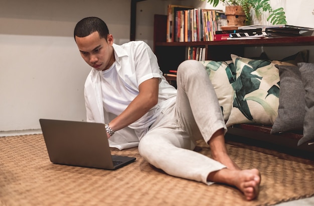 Home Living Concept An Asian man is lounging to use his laptop computer to shop online comfortably.