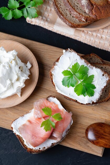 Home made bread on a wooden cutting board with curd cheese and salmon Decorated with green herbs