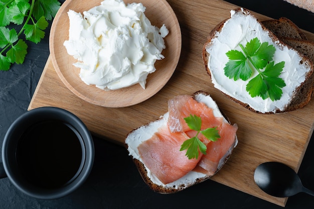 Home made bread on a wooden cutting board with curd cheese and salmon Decorated with green herbs