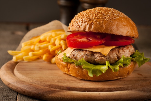 Home made hamburger with beef, onion, tomato, lettuce and cheese. Fresh burger close up on wooden rustic table with potato fries, beer and chips. Cheeseburger.