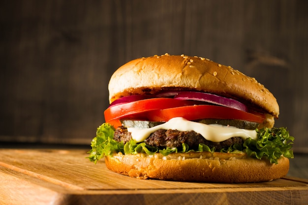 Home made hamburger with beef, onion, tomato, lettuce and cheese. Fresh burger close up on wooden rustic table with potato fries, beer and chips. Cheeseburger.