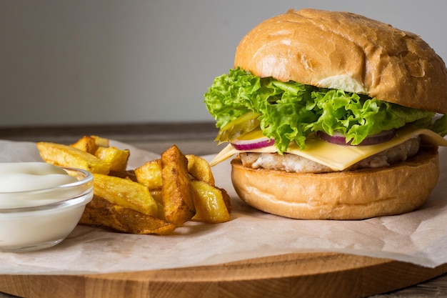 Home made hamburger with chicken onion cucumber lettuce and cheese on wooden rustic table with potato fries